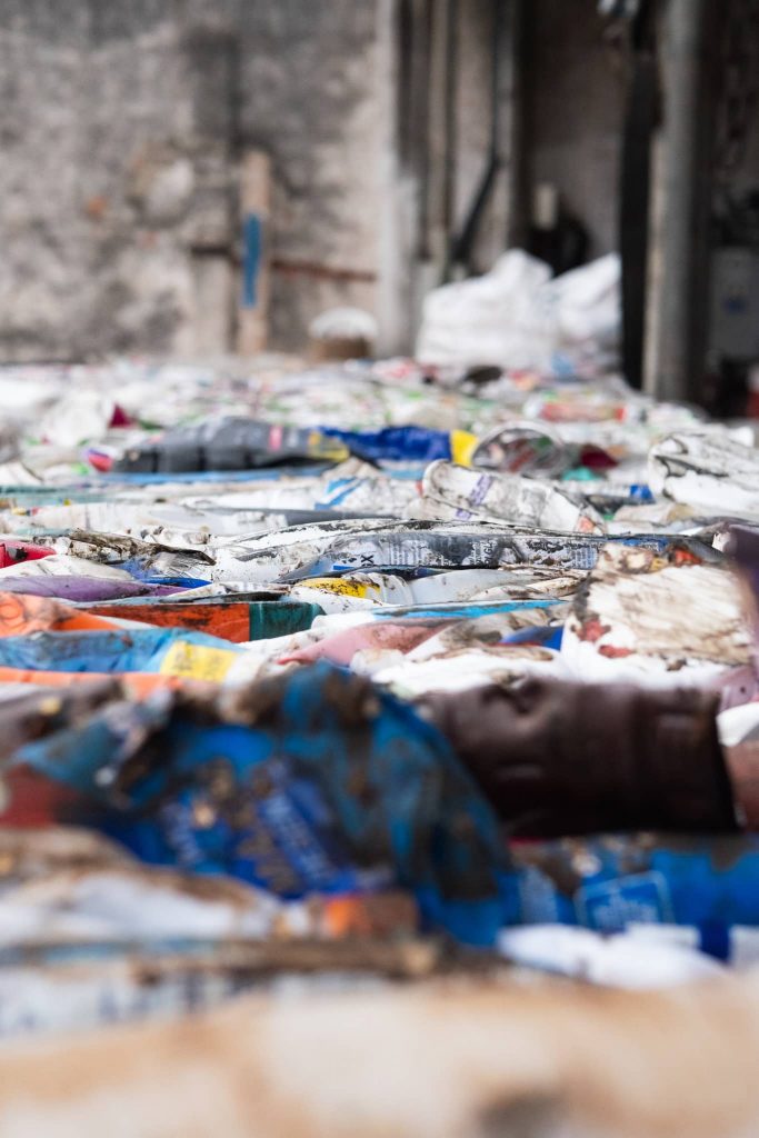 A large accumulation of compressed waste materials, primarily consisting of various types of recyclables, such as paper, cardboard, and plastics. The focus is on the textures and colors of the different layers of waste, with the depth of field set to blur the background, drawing attention to the waste in the foreground.